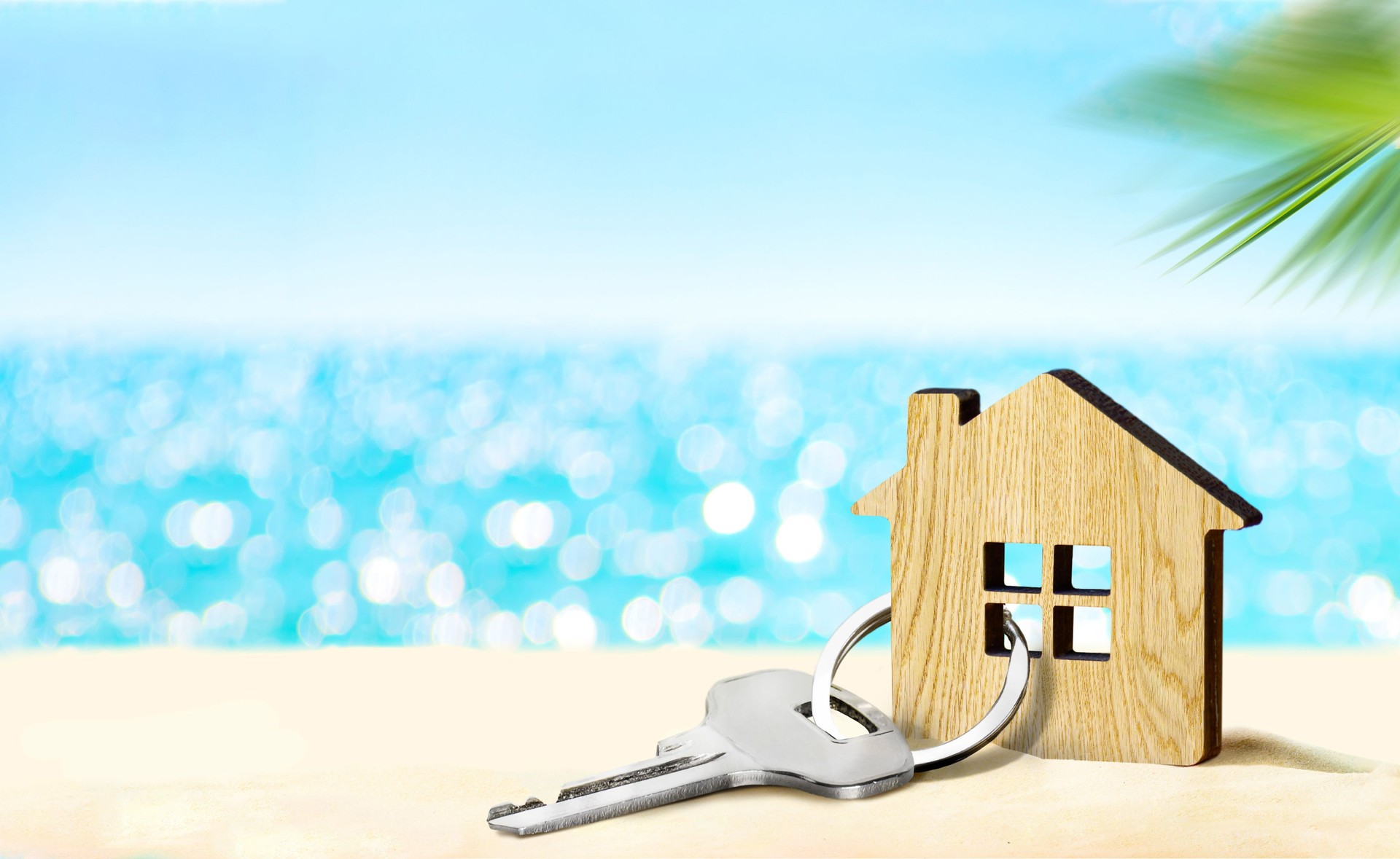 House by the sea concept. Figure of house and key on sandy beach